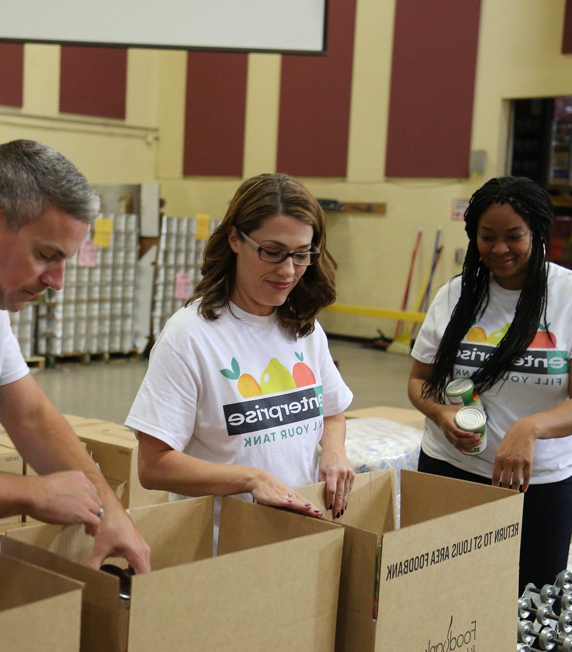 两名女性企业员工和一名男性员工, 都穿着白色的企业号加油t恤, 在社区服务项目中打包箱子.