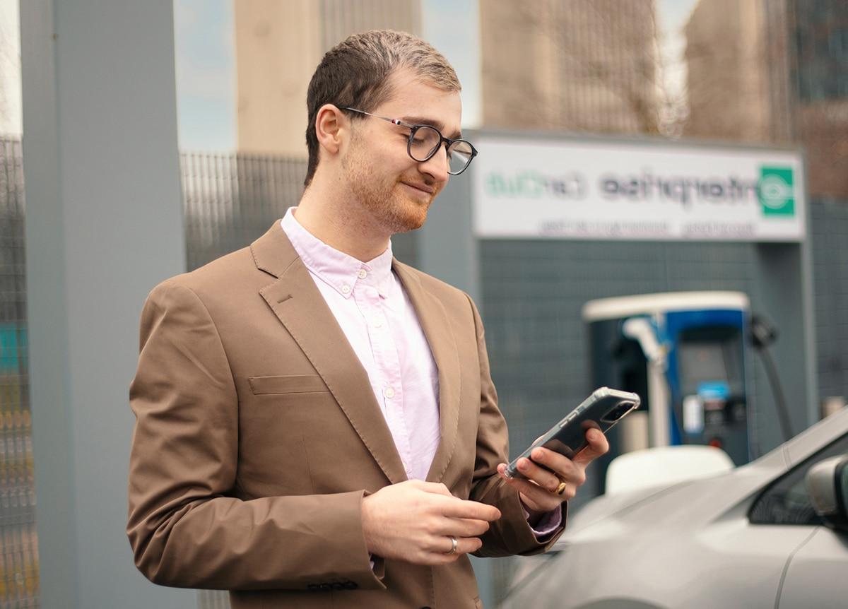 一个穿着职业装、皮肤苍白、戴着眼镜的男人站在外面，低头看了看手里拿着的手机, 柔和的微笑.